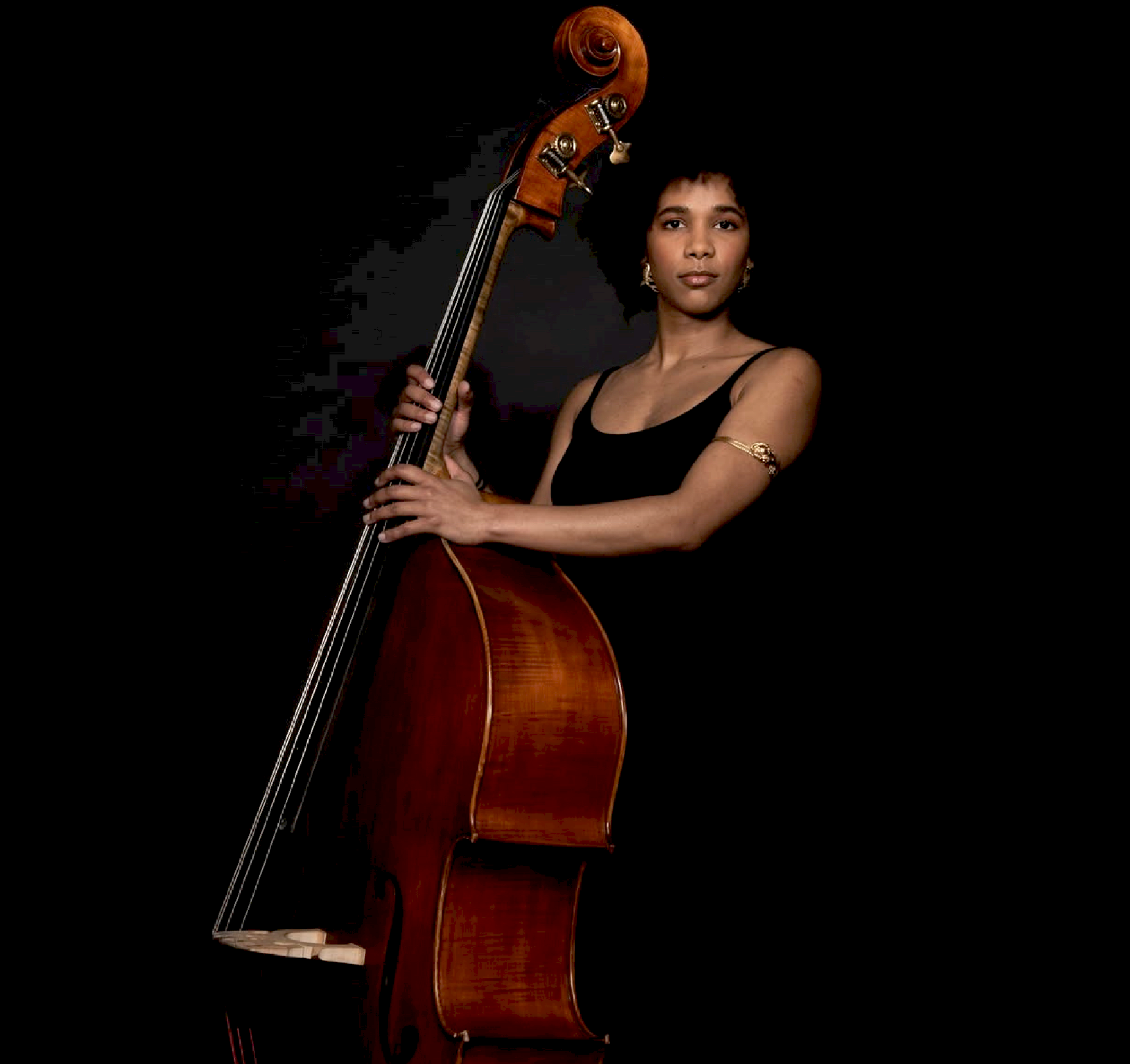 Double bassist standing with her instrument against a black background